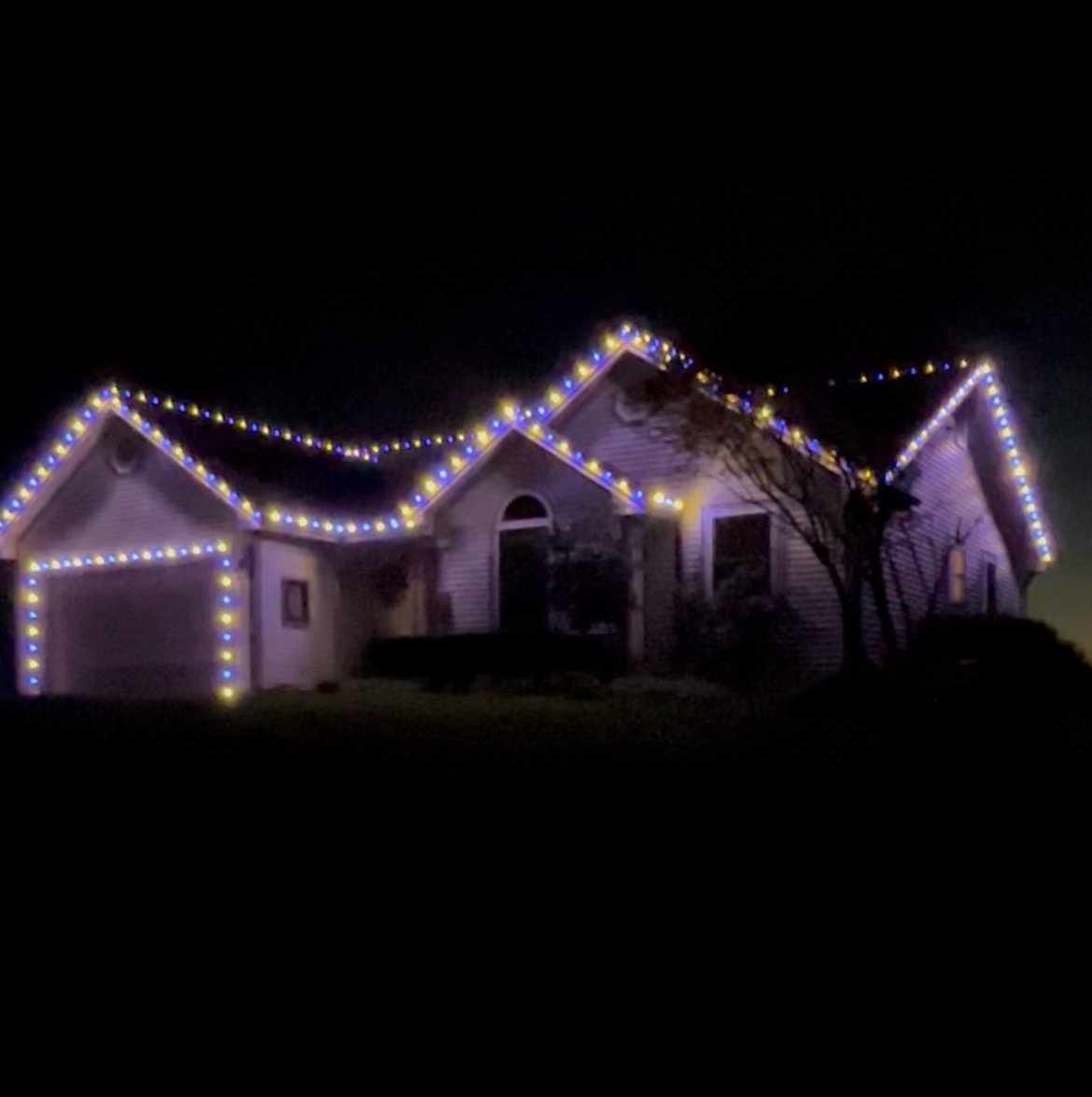 House illuminated with purple and white string lights outlining the roofline, garage, and edges at night