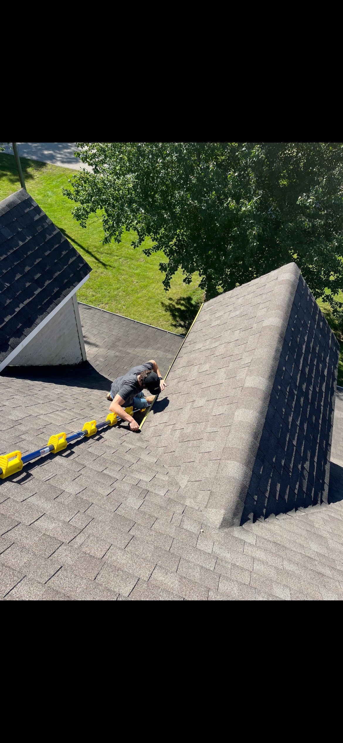 Person climbing a steep outdoor concrete structure with yellow safety rope, grassy field and trees visible below