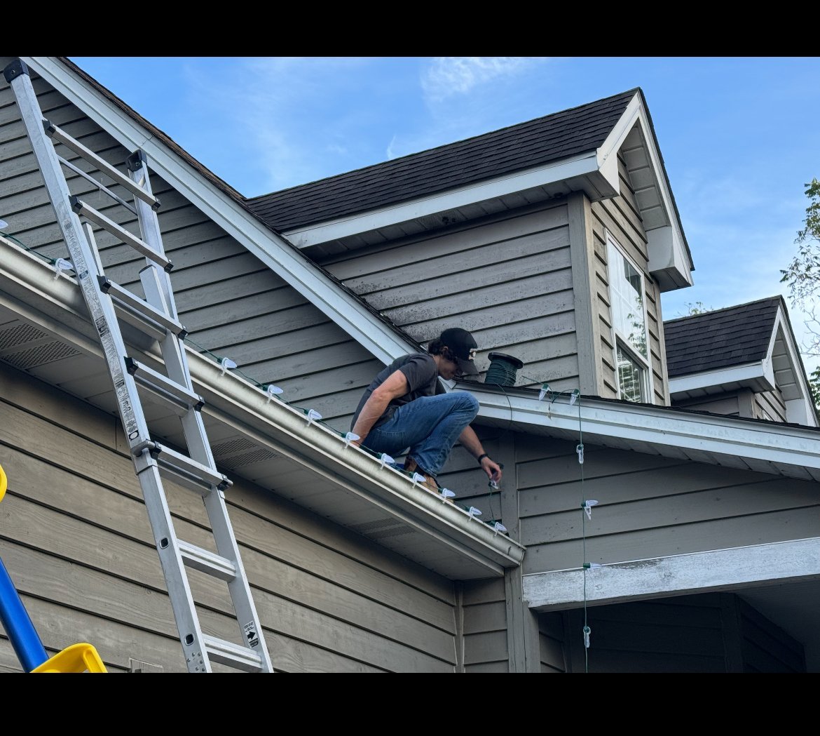 Person on ladder working on residential house roof and gutters against blue sky