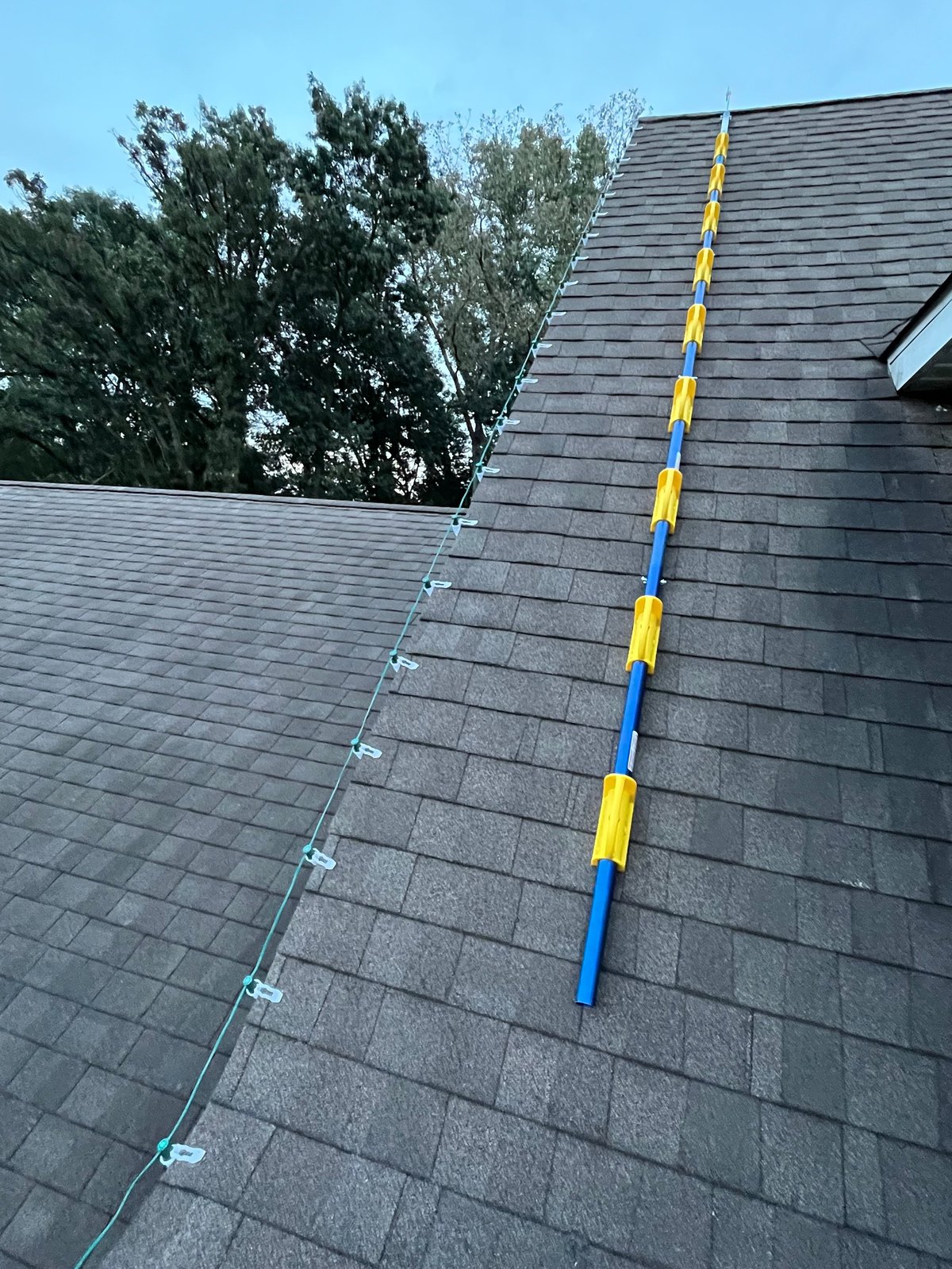 Roof with gray shingles showing safety rope and blue-yellow striped ladder climbing up steep residential roof