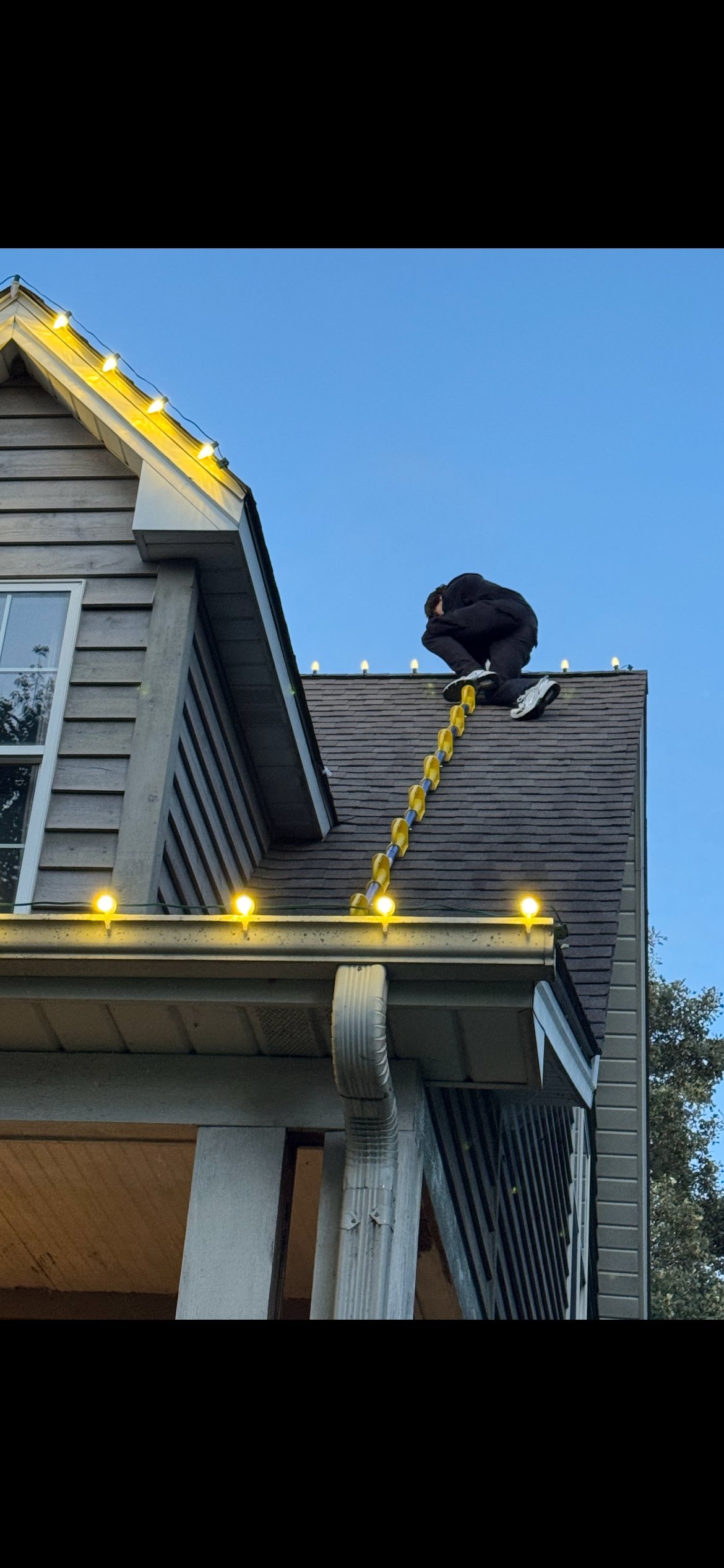 Person sitting on roof of modern house with yellow rope ladder and blue sky background